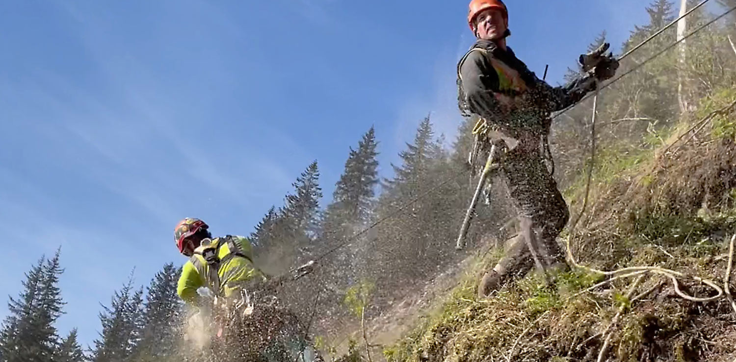 two crew members are held by cable as they clean up along the mountainside