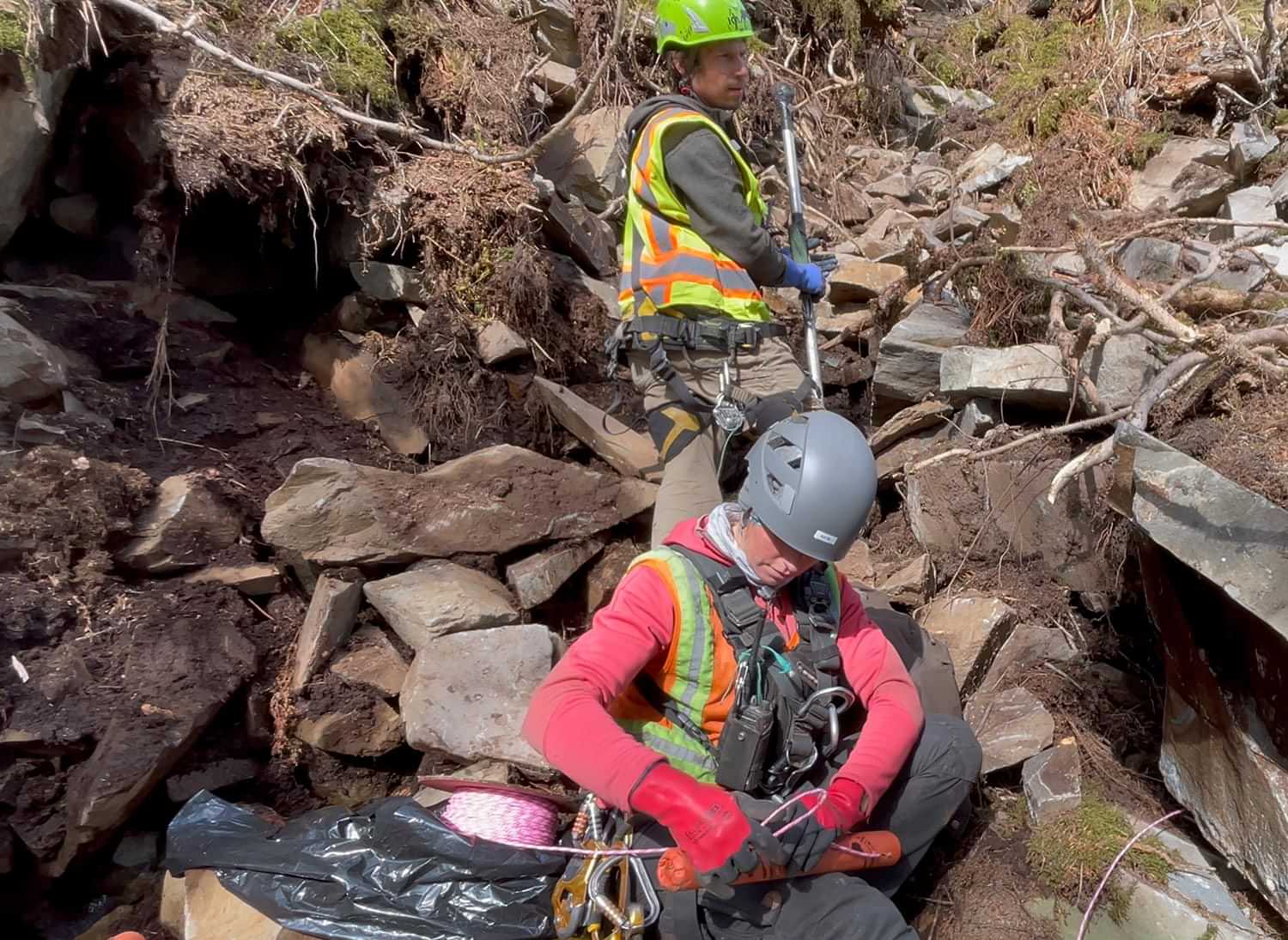 two clean up crew members stand among many rocks and boulders