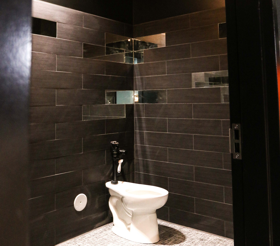 bathroom corner with toilet surrounded by brown tile with select tile pieces being reflective