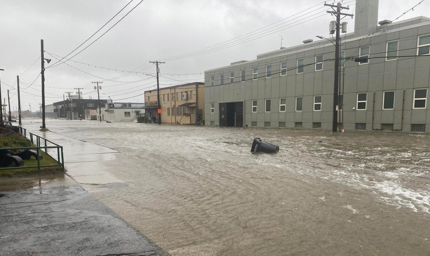 a wide flooded street in Western Alaska, a trash can sits in the middle of the street almost submerged
