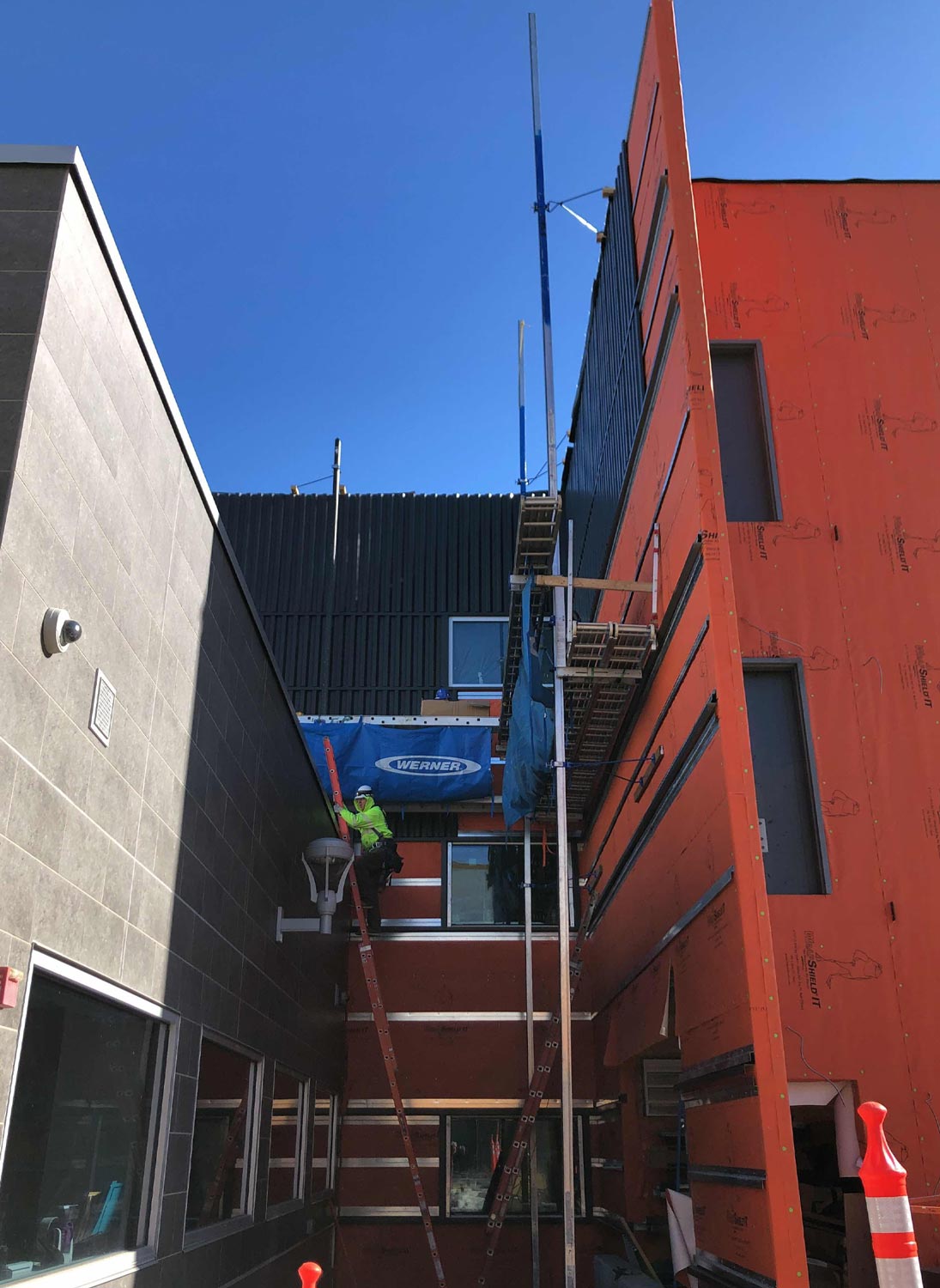distant view of a construction worker standing toward the top of a ladder in a space between two buildings