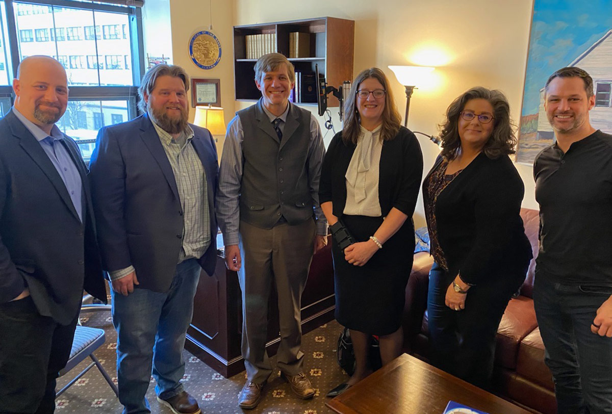 four male and two female AGC member attendees stand side by side in an office, smiling for a group photo at the 2023 AGC Alaska Legislative Fly-In event