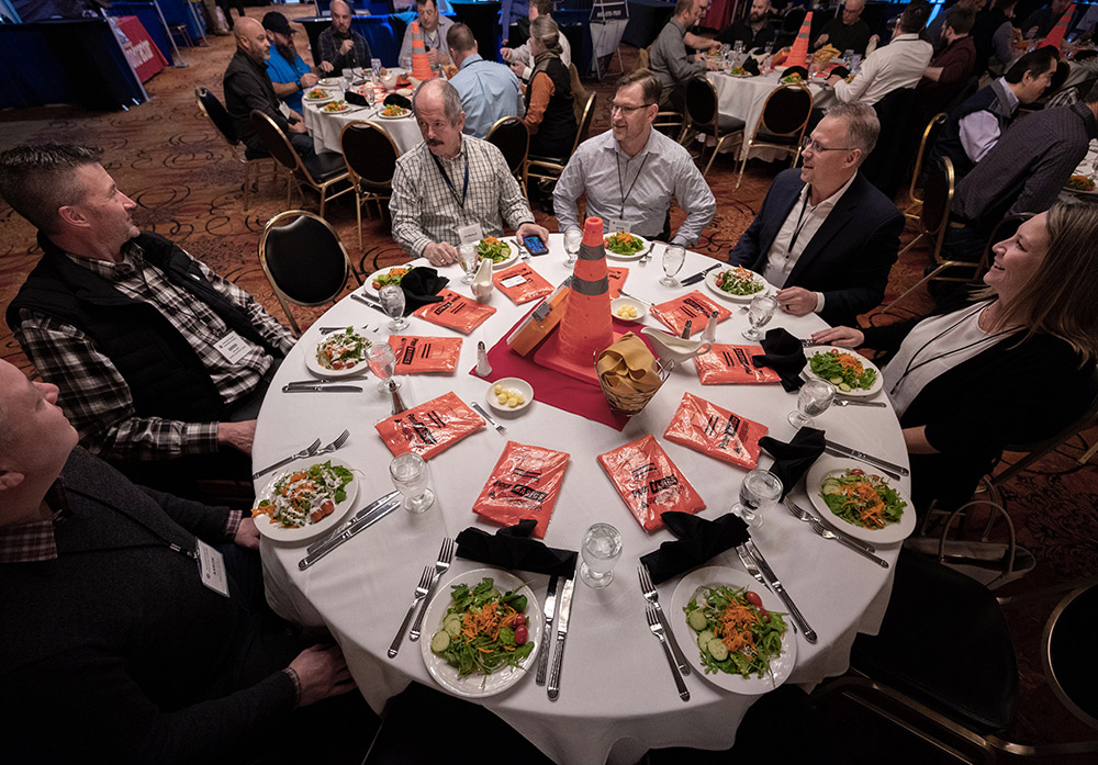 group of people at an event sitting around a circular table with salads