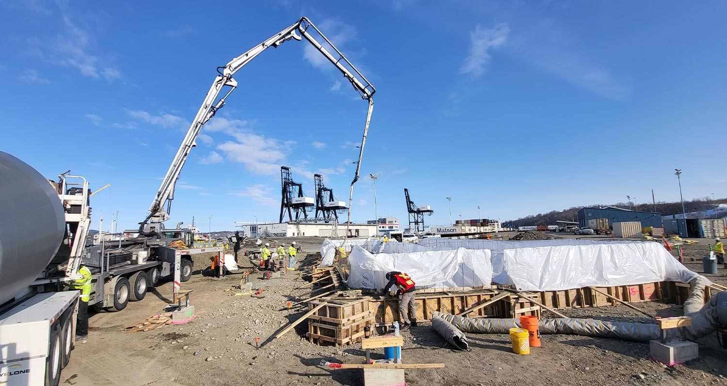 under a blue sky early work is done on the Port of Alaska administration building as workers supervise the pumping of concrete