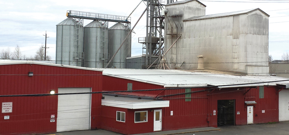 Alaska Mill and Feed’s feed mill and warehouse facility, red building with tall white building and grain silos in the background