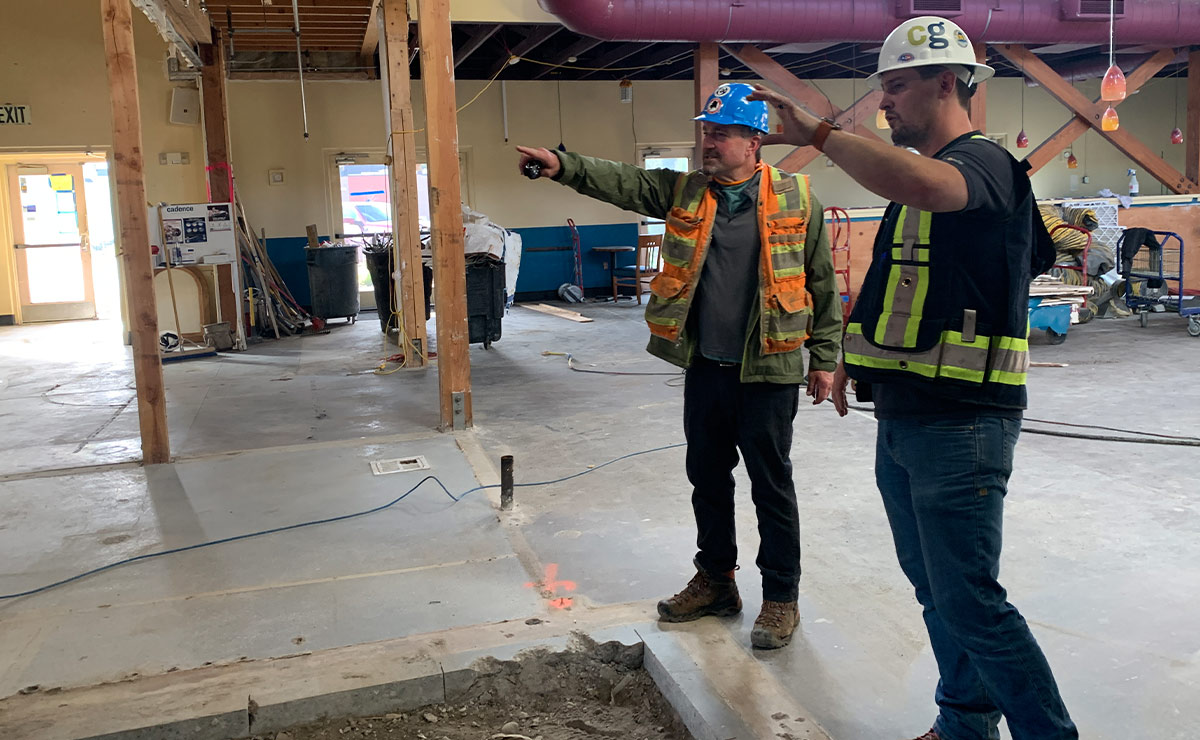 two men wearing safety vests and hard hats stand in the new Moose’s Tooth location in South Anchorage