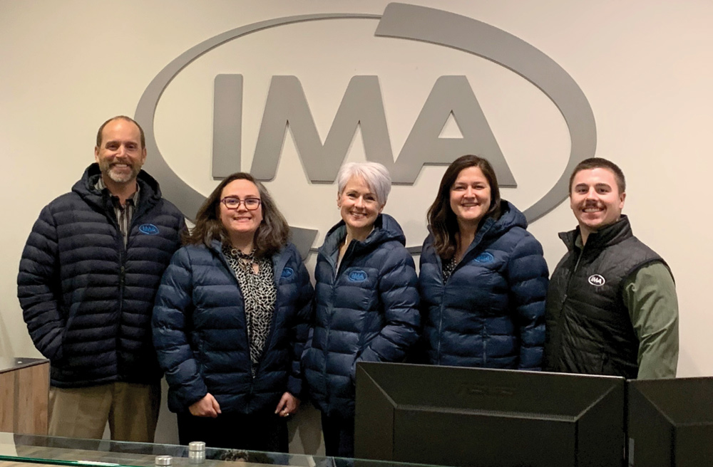 group of people standing in from of an IMA sign