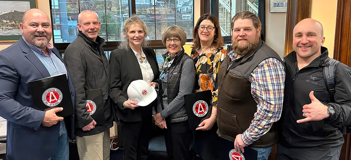 seven people in an office holding AGC folders and a hard hat