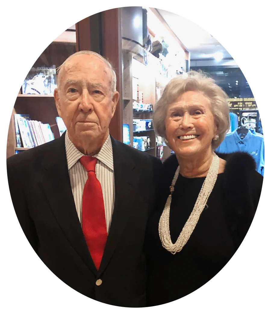 Herbert Lang wearing a black suit with a red tie and posing beside Marianne Pfeil Lang wearing a black dress and multiple strands of pearls