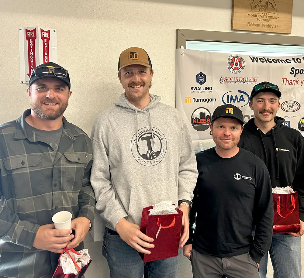 Four men posing with red gift bags at the 2025 AGC of Alaska Sporting Clays Shoot