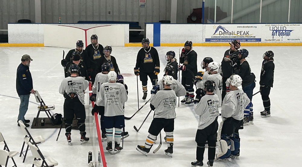 Hockey players in black and white jerseys gather in a circle on the ice for a team meeting or instruction during the 2026 Contractors vs Camo event.