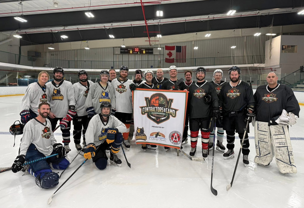 A smaller group of hockey players from both teams pose together on the ice holding a "Contractors vs Camo" banner presented by AGC of Alaska and Challenge Alaska.