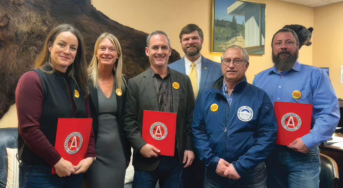 Six smiling professionals pose indoors together, with several holding red folders featuring a circular logo, in front of a mounted animal hide.