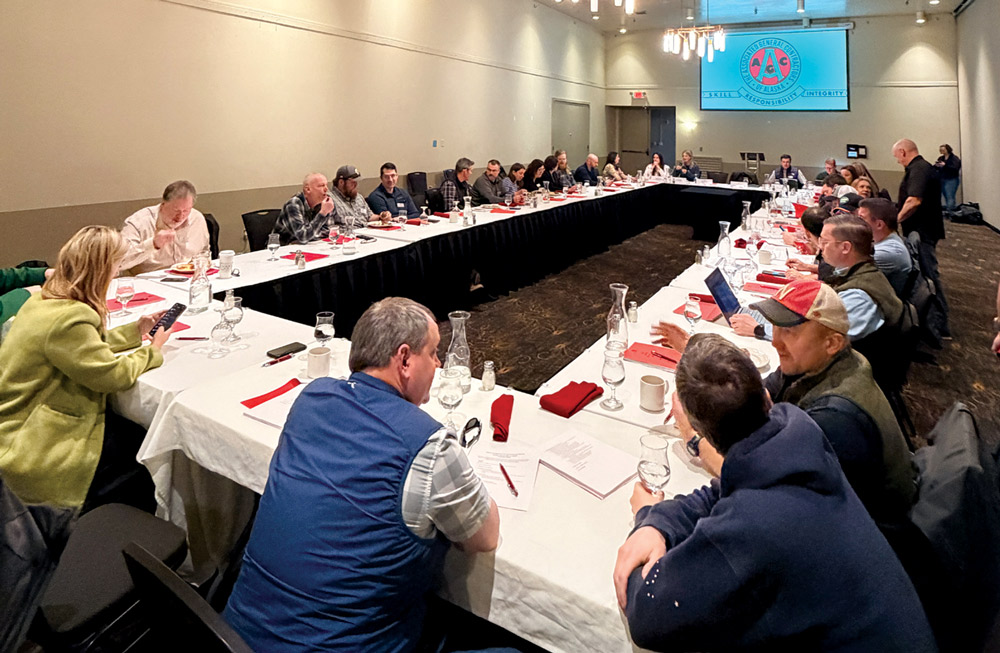 Attendees sit along a large U-shaped conference table during a meeting with an AGC presentation on the screen.