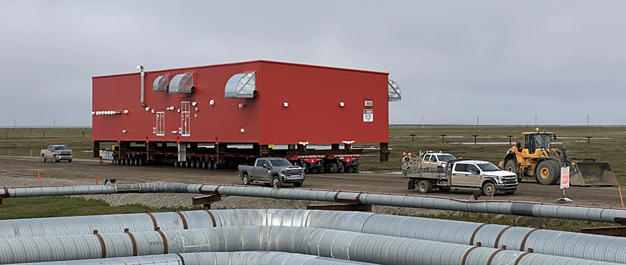 Barge with cargo containers and machinery on a shore; a crane and Volvo dump truck on beach.