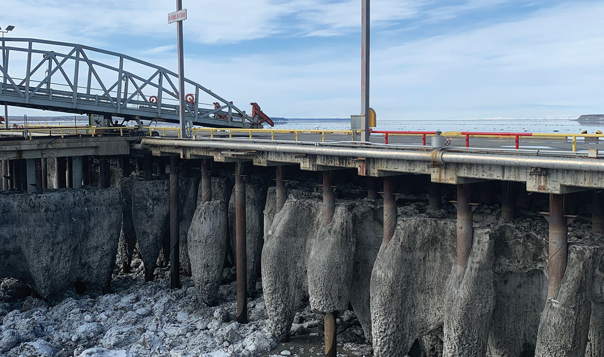 Industrial pier supported by metal pillars rising above a frozen, ice-packed coastline.