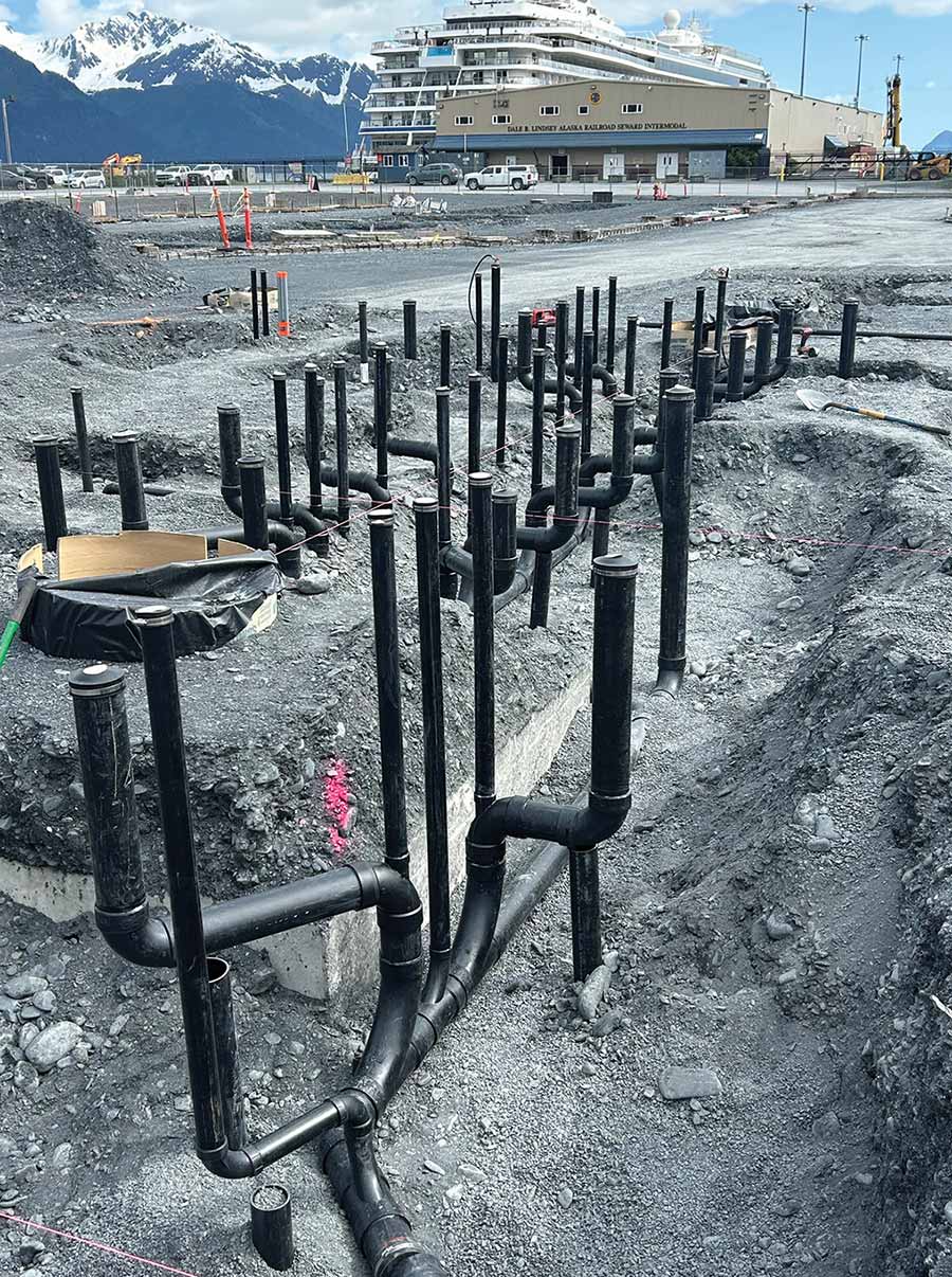 A network of black utility pipes installed in a dirt trench outdoors.