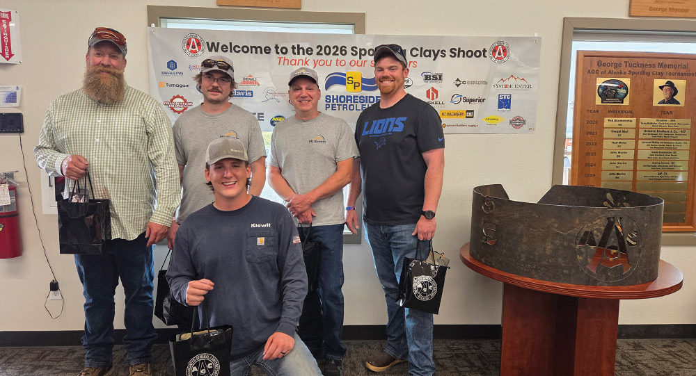Group of five men holding black gift bags posing indoors in front of a sponsor banner.