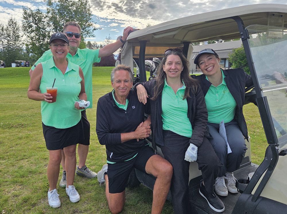 Group of five smiling golfers wearing matching bright green shirts posing together around a golf cart.