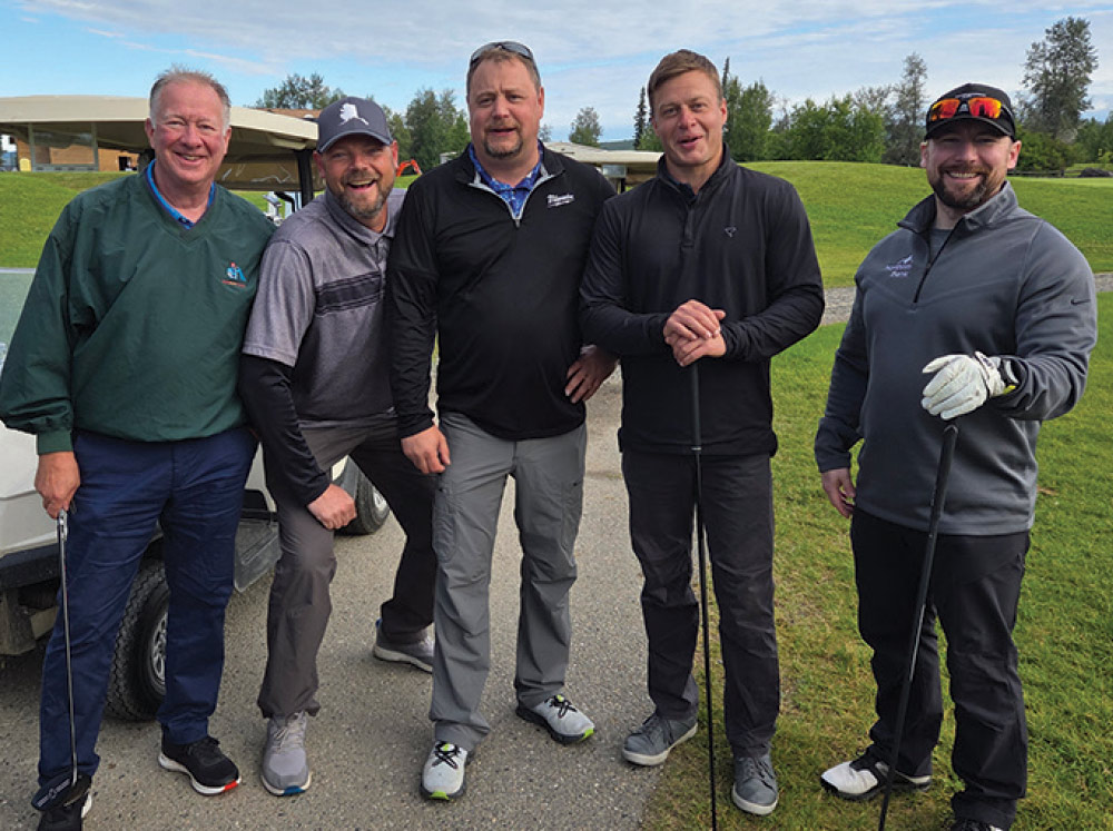 Five male golfers in casual athletic wear standing together on a paved path on the course.