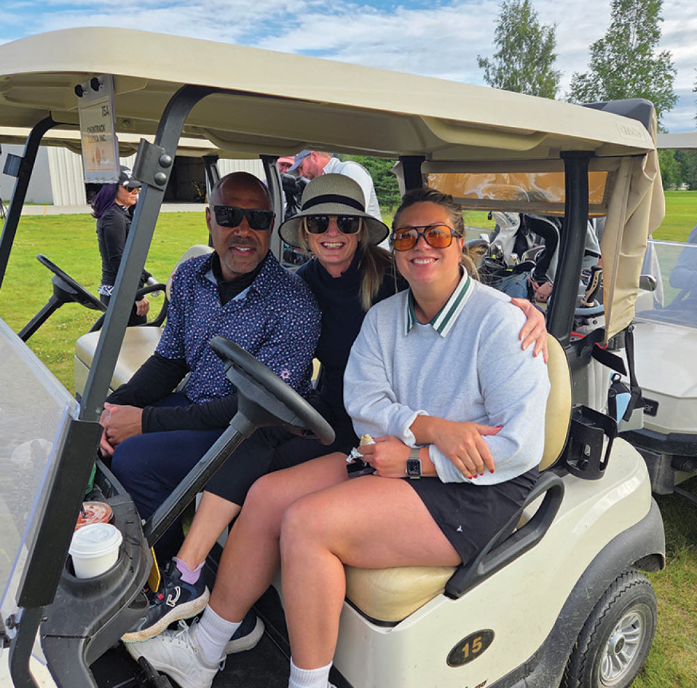 Three smiling golfers sitting together inside a white golf cart on the course.