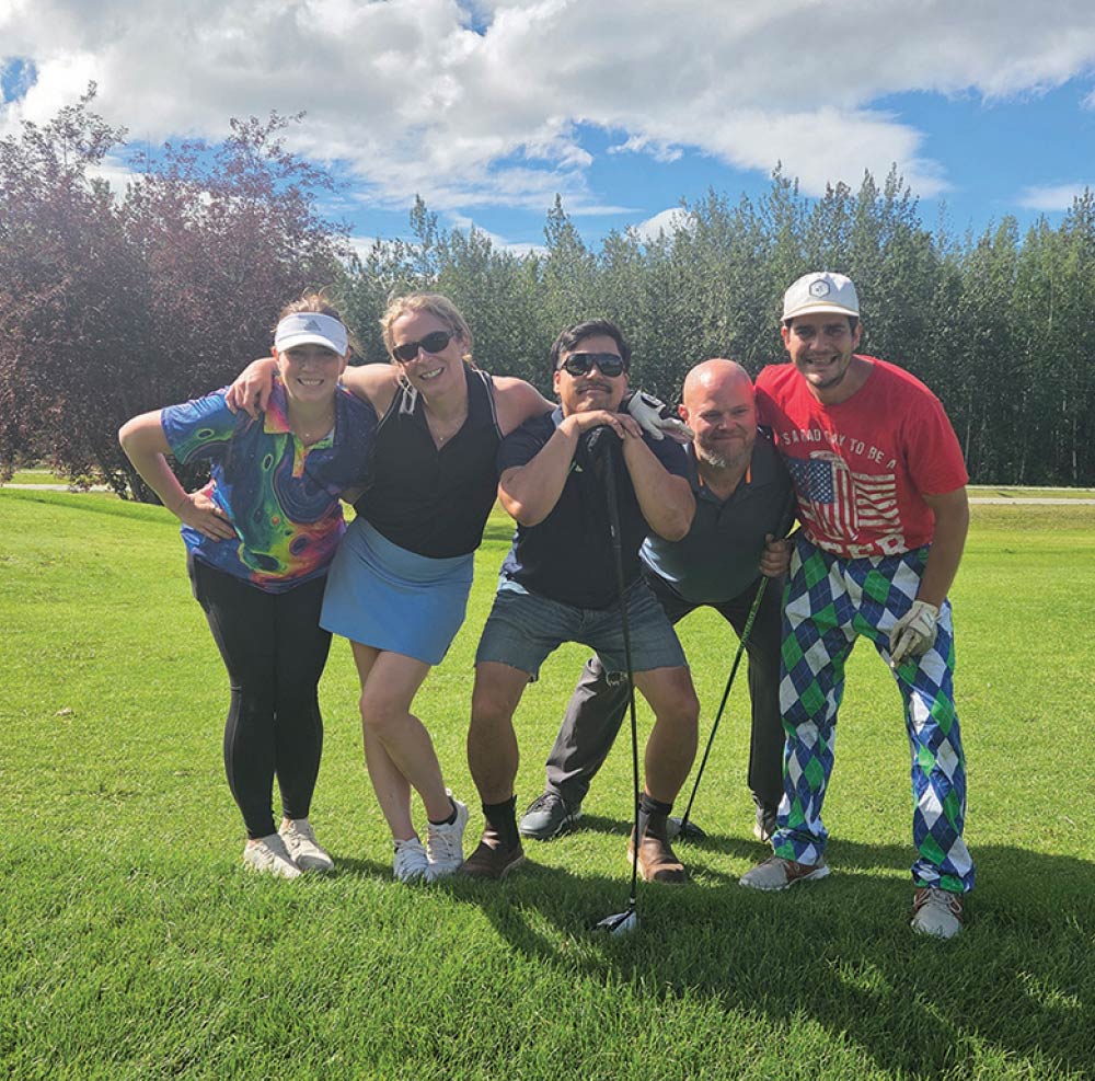 Five golfers in fun outfits leaning in close and smiling for a group photo on the lawn.