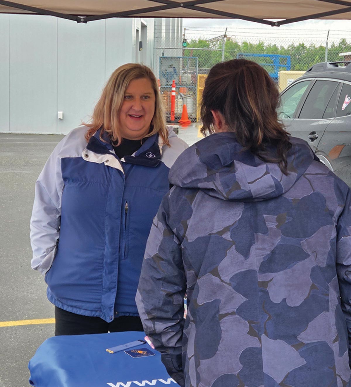 Two women chatting comfortably under a pop-up tent during a rainy outdoor gathering.