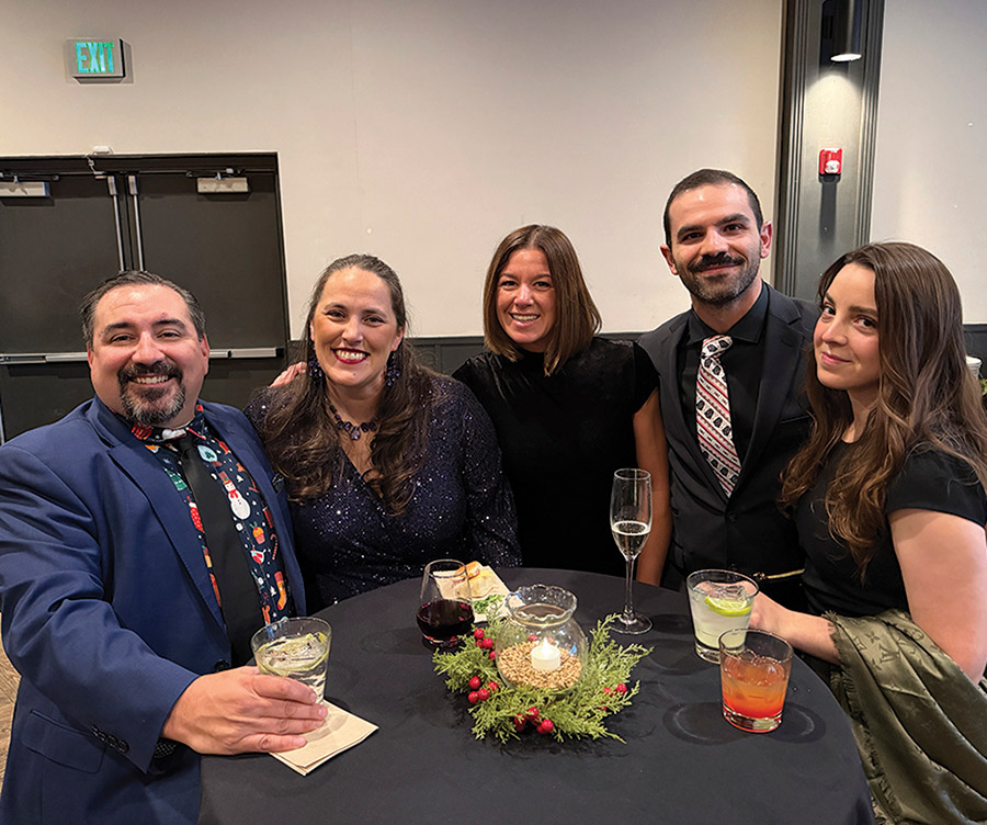 Five people smiling together around a high-top table at a formal evening event.