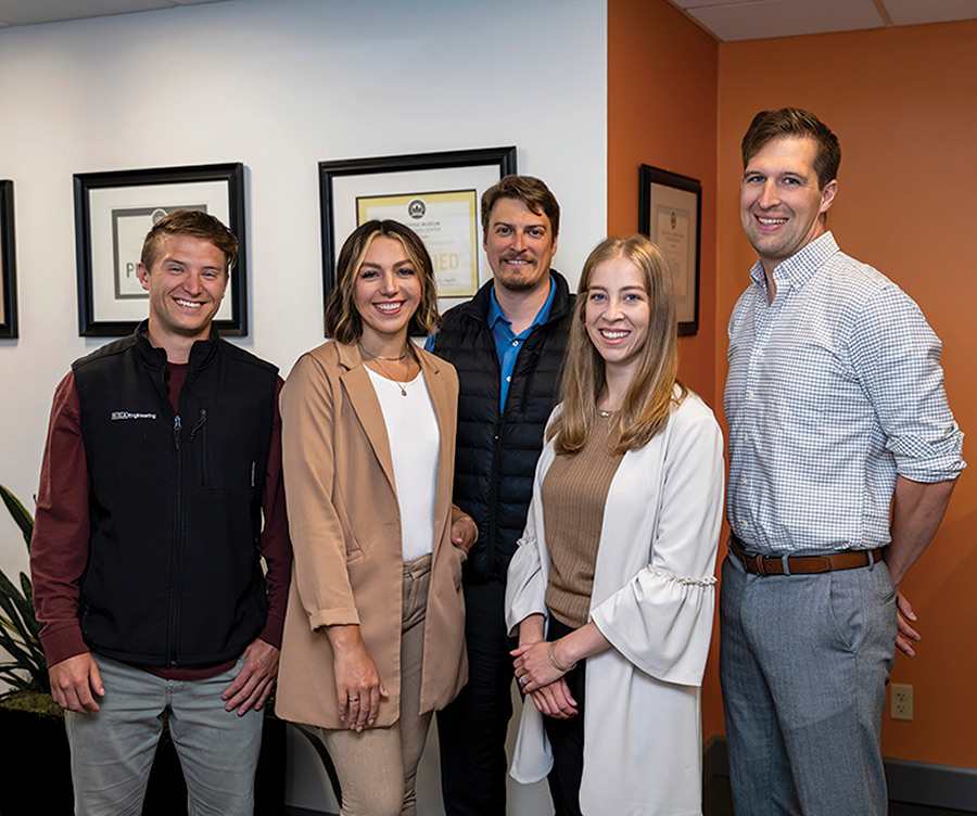 Five professionals standing together in an office hallway posing for a team photo.