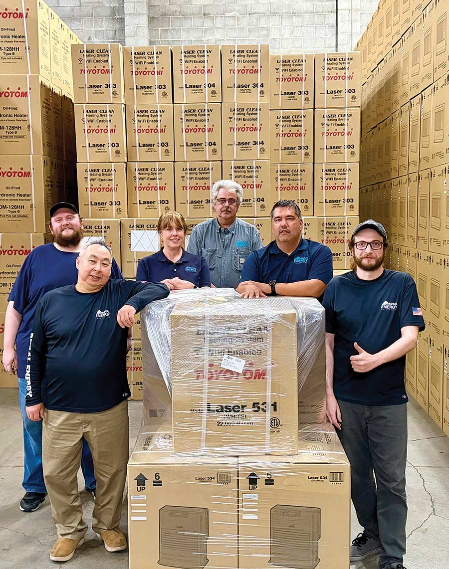 A group of workers posing together in front of stacked boxes in a warehouse.