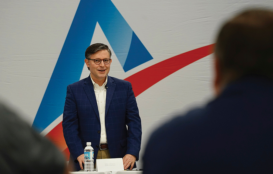 A man in a blue suit speaking at a podium before an audience.
