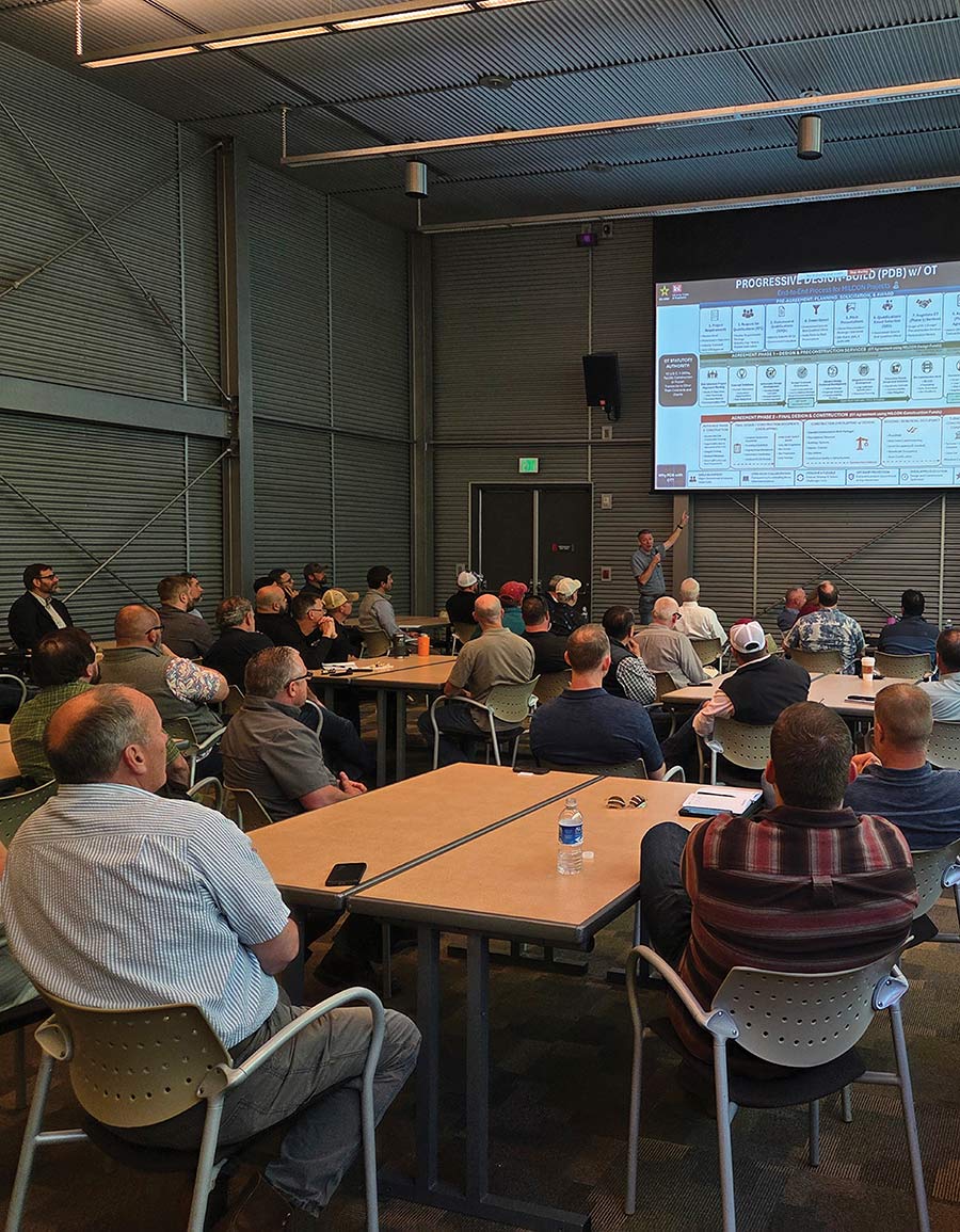 An audience watching a presentation projected onto a screen inside a large hall.